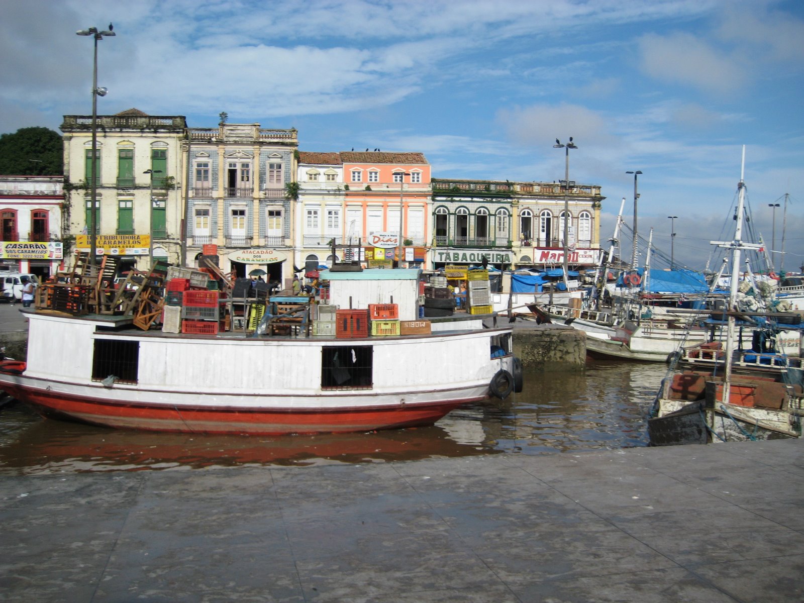 Small river fishing boats pulled up to a concrete dock in front of brightly colored colonial era buildings.